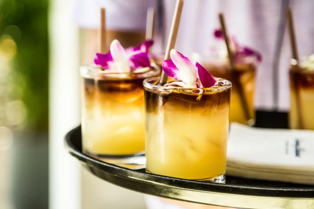 Four layered cocktails with ice and purple orchid garnishes are served on a tray with a stack of napkins, ready for the photoshoot under the creative direction of a skilled creative director.